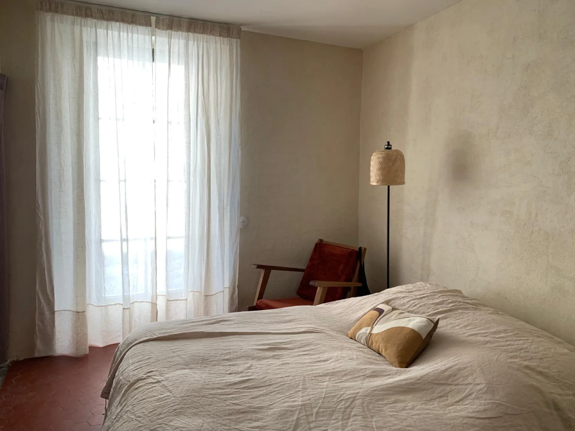 Chambre double avec voilages blancs et fauteuil en bois