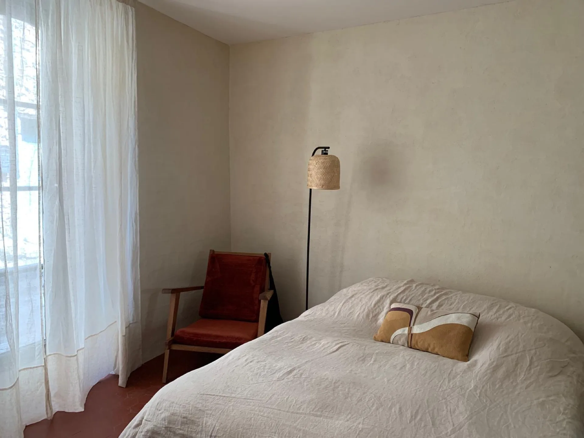 Chambre double lumineuse, fauteuil rouge, lampadaire en rotin